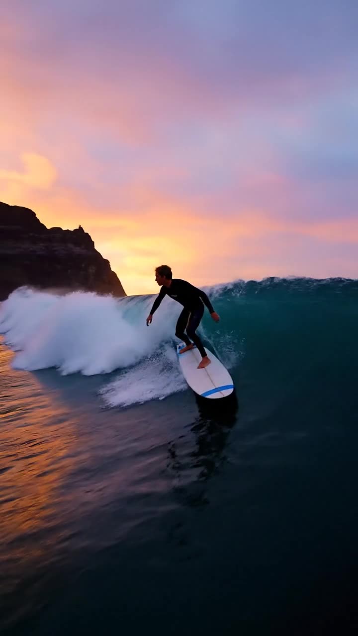 A surfer rides through sunset spray in a vertical tracking shot with synchronized ocean sound
